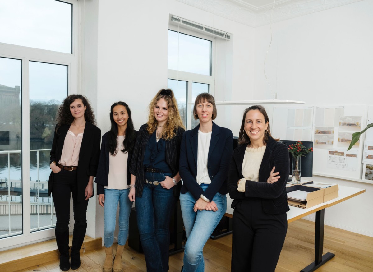 Team STADTCONTUR Architekten 01 Foto der Architektinnen im eigenen Büro mit schönem Ausblick auf die Weser. Wir haben moderne Arbeitsplätze in hellen Räumen mit Stuck und Holzdielen und höhenverstellbaren Schreibtischen mit zwei Bildschirmen. Wir sind voll digital ausgestattet und arbeiten mit 3D-Software und KI-Bildgeneration.